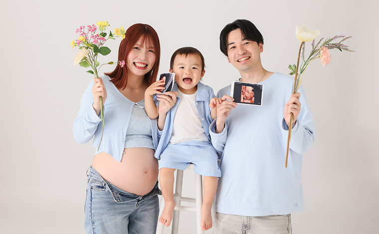 マタニティドレスを着た妊婦さんがブーケを持って立っている写真